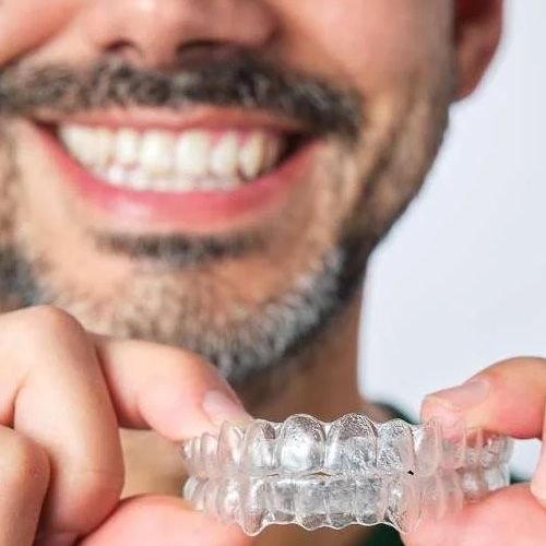 smiling man holding invisalign clear plastic aligners | invisalign dedham ma